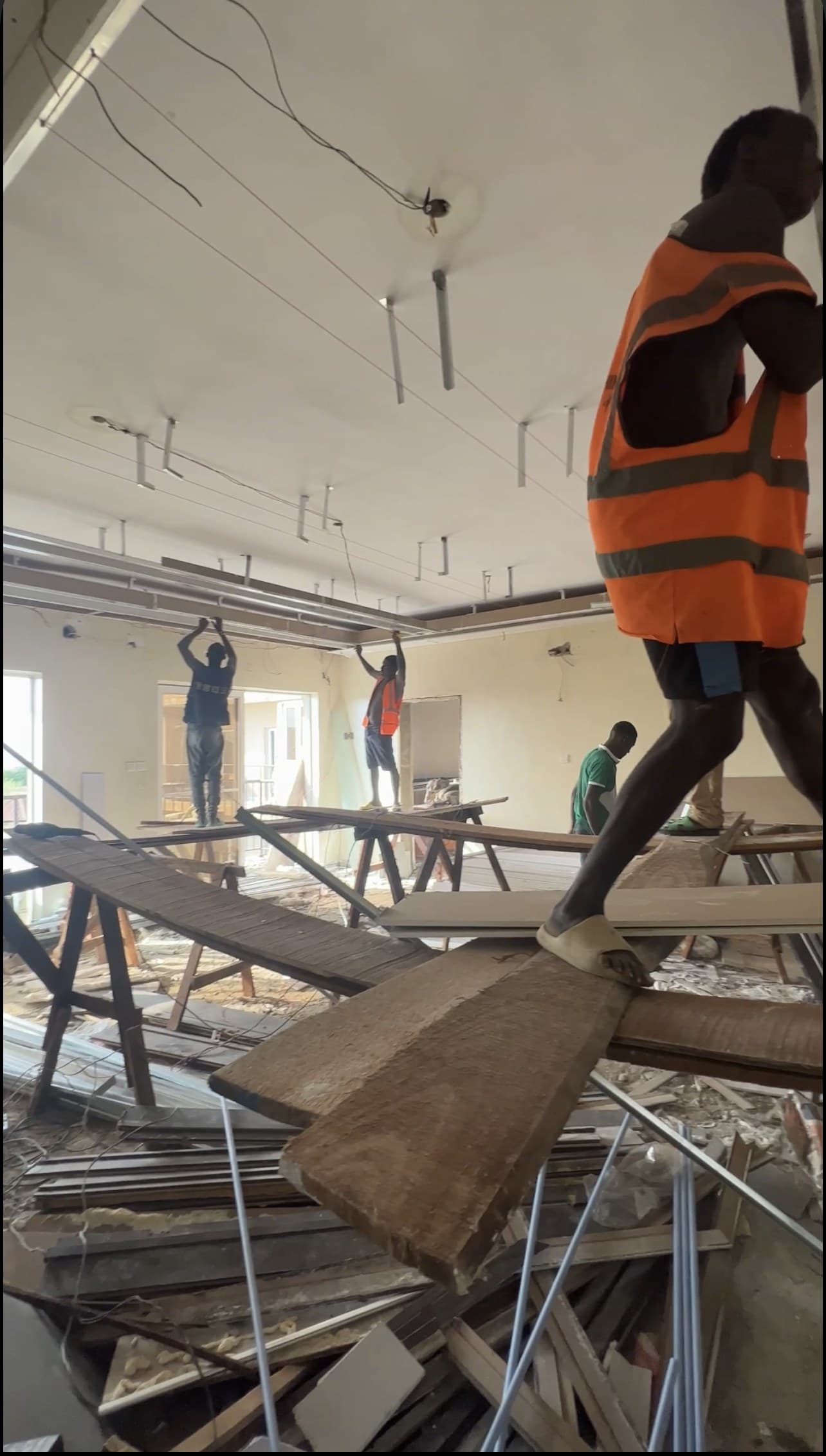 The property mid-renovation, workers on makeshift plank scaffolding fitting a ceiling, debris on the floor