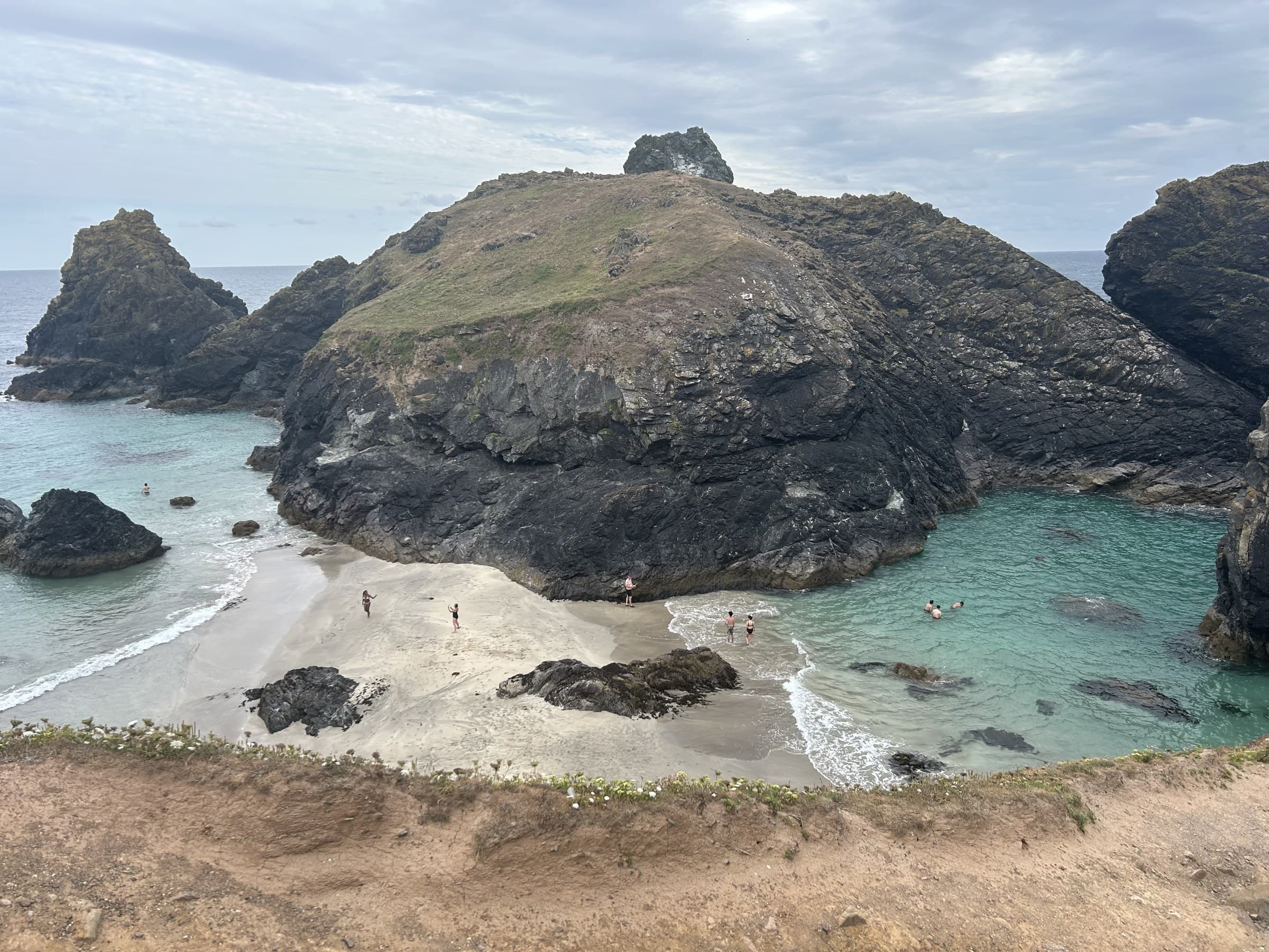 Kynance Cove's beach between its rock stacks, visitors swimming and walking